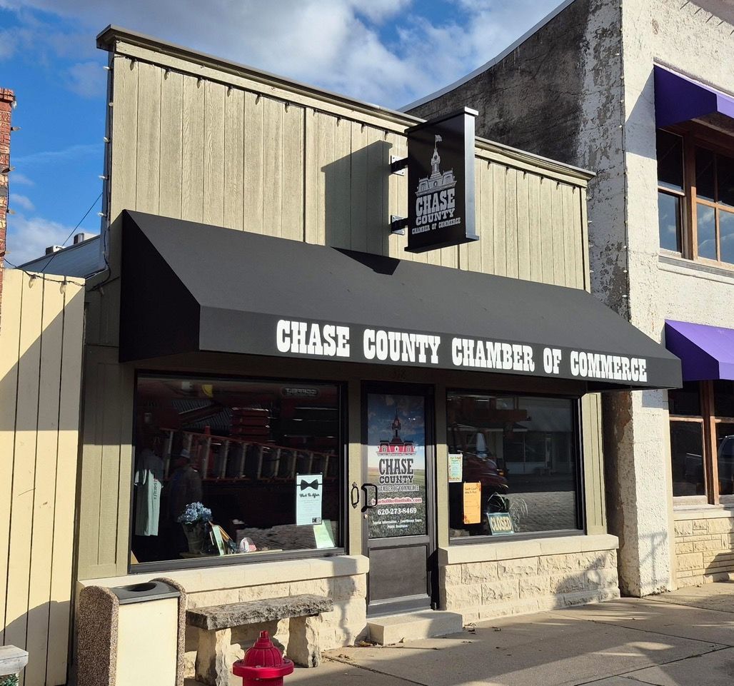 Chase County Chamber of Commerce storefront with black awning and signage, concrete bench, and red fire hydrant.