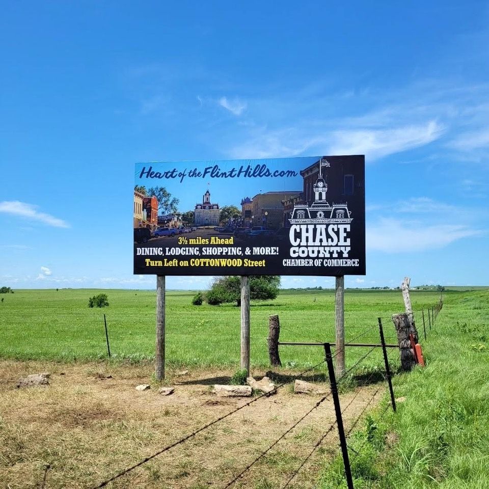 Billboard promoting Chase County, Kansas, in a field, under a blue sky.