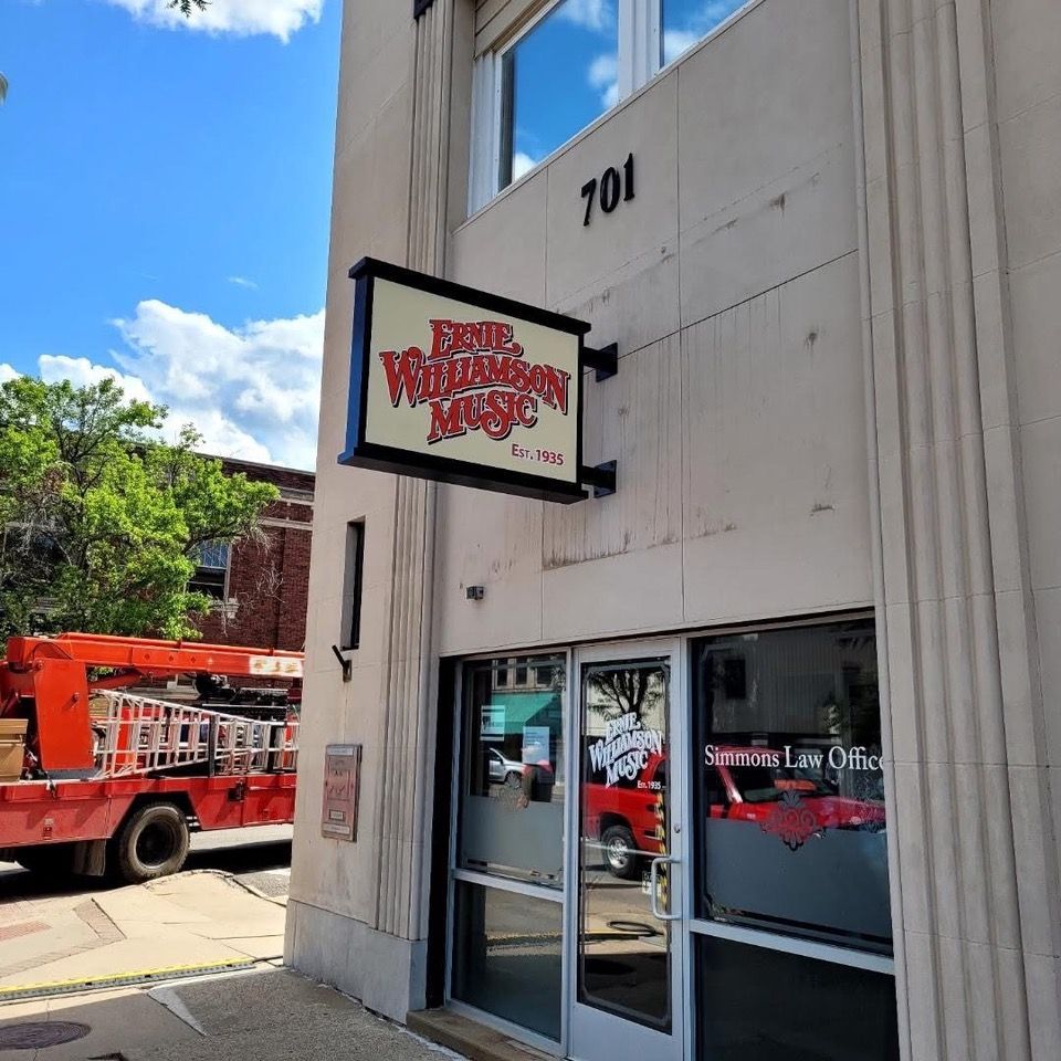 Exterior of 'Brad Williamson Music' shop with sign, building number 701. Red construction truck nearby.
