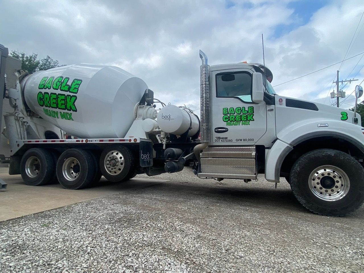 White Eagle Creek cement truck parked on gravel, cloudy sky in background.