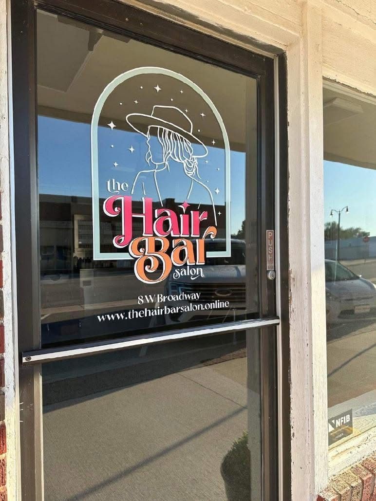 Glass door of 'The Hair Bar' salon with logo and website.