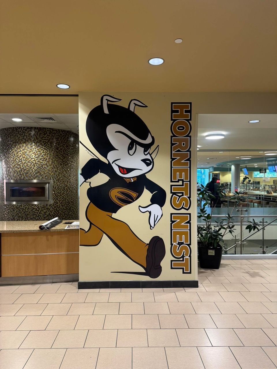 Mural of a cartoon hornet mascot running on a wall; 'HORNET'S NEST' text. Tan, black, brown and orange.