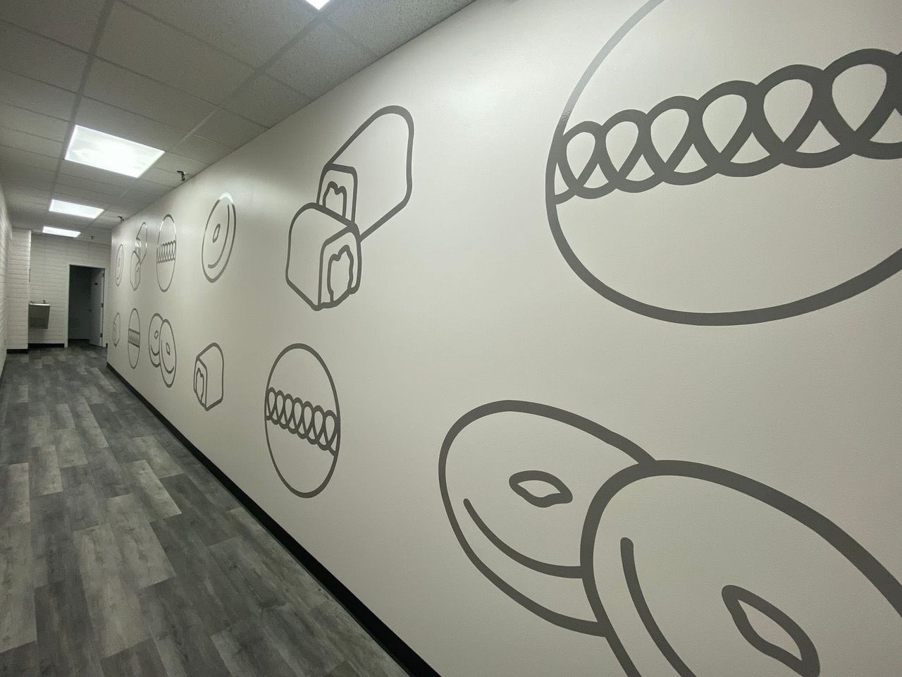 Long hallway with white walls featuring dental-themed illustrations in gray, gray flooring, and recessed lighting.