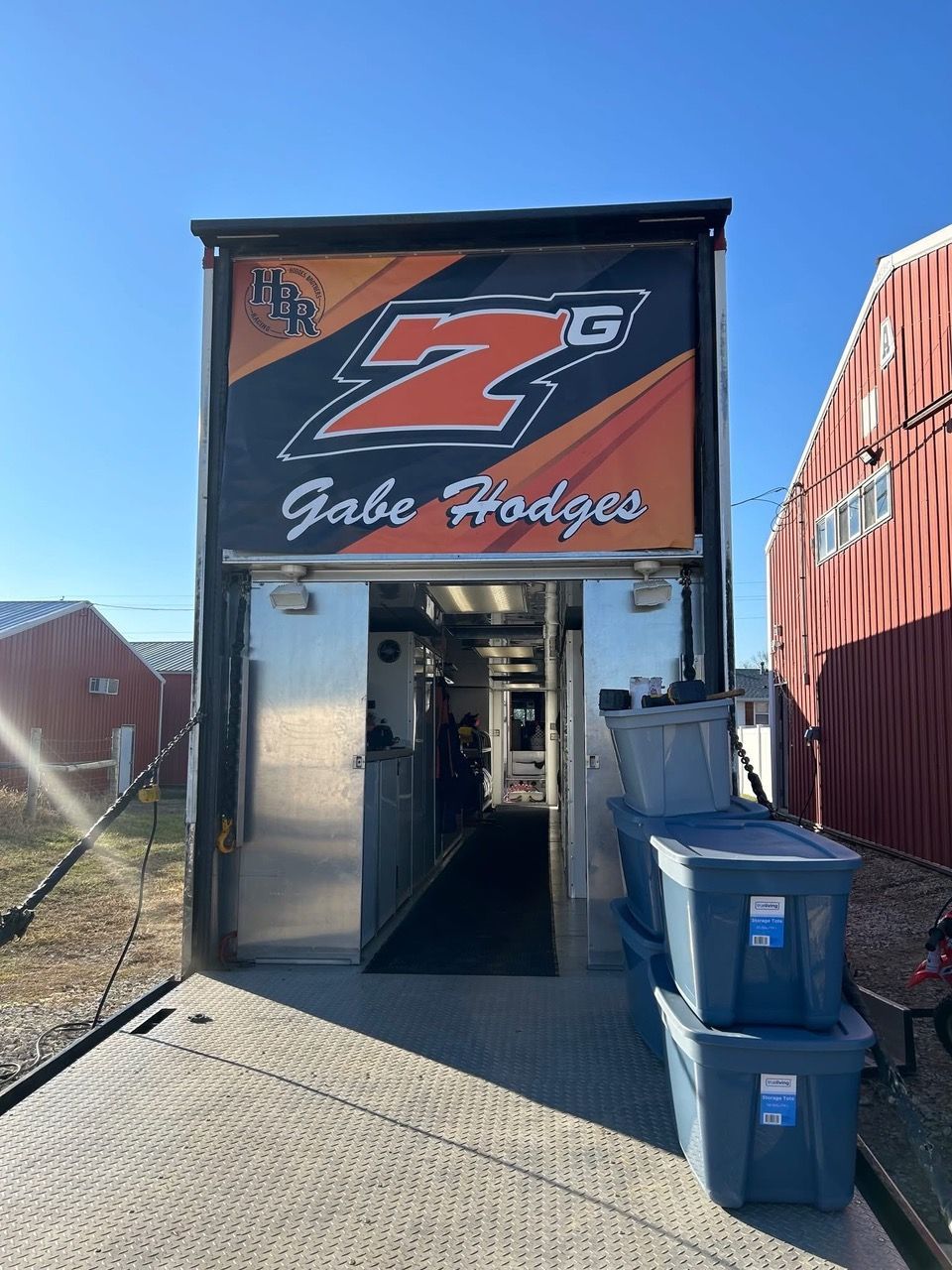 Race trailer with orange 'ZG' logo and 'Gabe Hodges' name, open doorway, blue bins.
