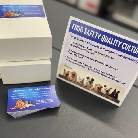 Stacks of white product boxes, a sign about food safety, and a stack of business cards with a logo and pet illustrations.