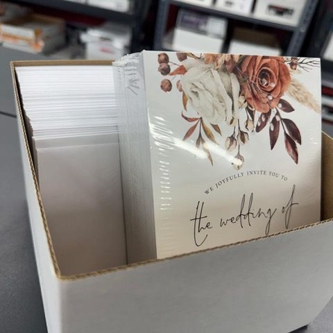 Box of wedding invitations, floral design, stacked with envelopes, in a white box.