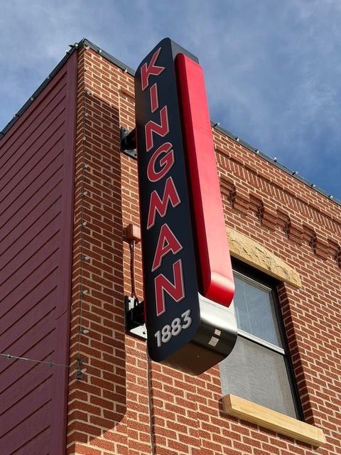 Sign for Kingman, Arizona, with the town's name, year 1883, and a red-trimmed, black sign against a brick building.