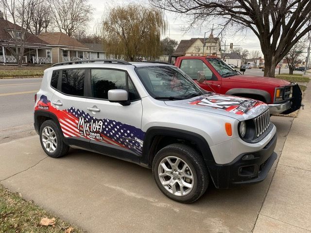 Silver Jeep Renegade with American flag wrap parked next to a red truck on a residential street.