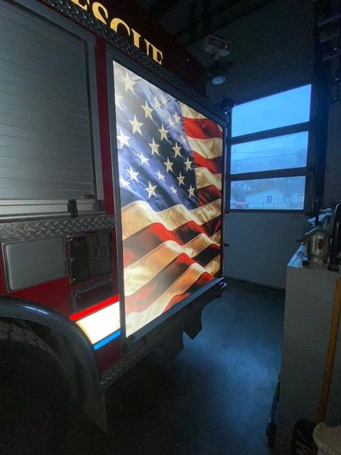 Fire truck with illuminated American flag, parked inside garage, blue window in background.