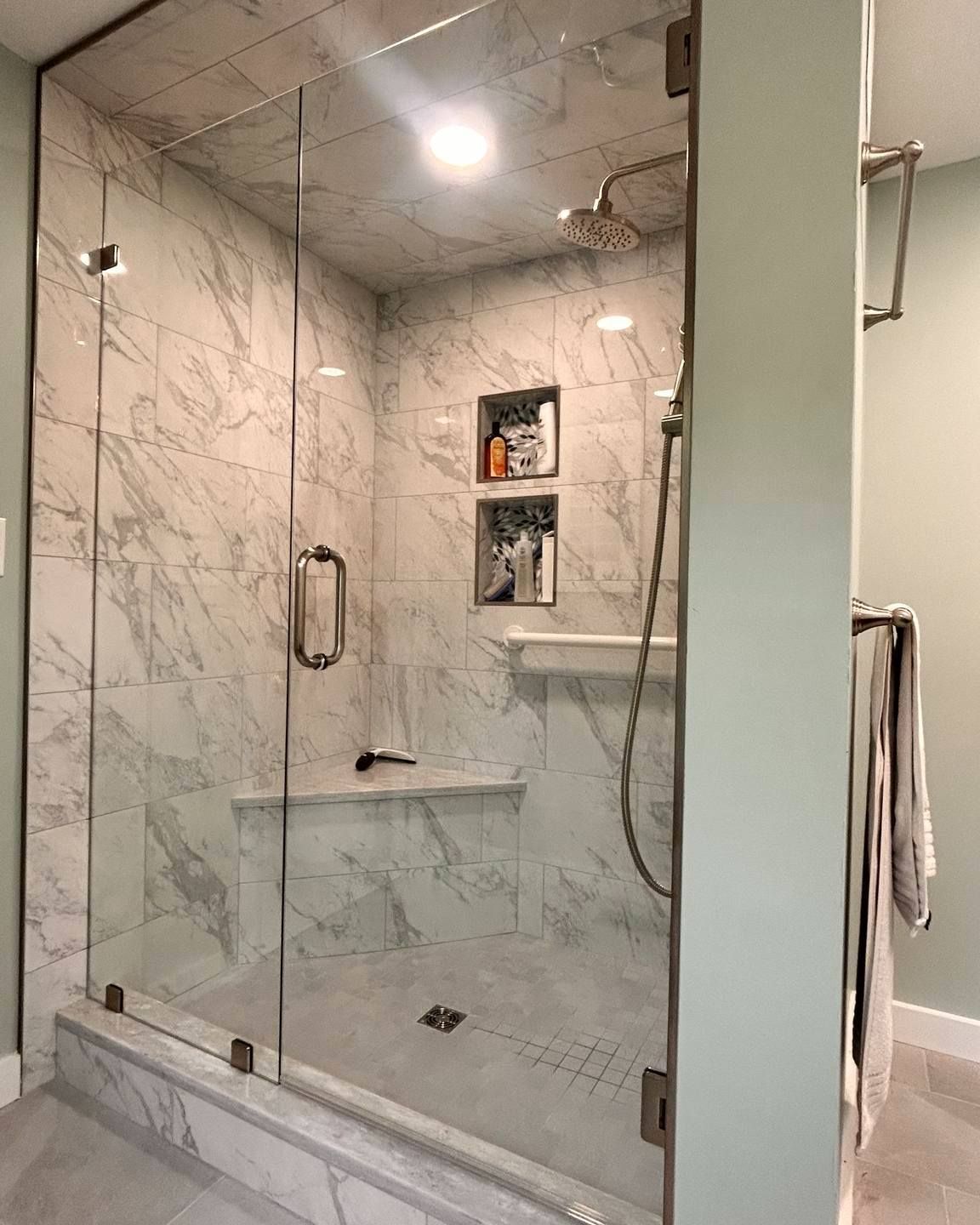 A bathroom with a walk in shower with a glass door and marble walls.