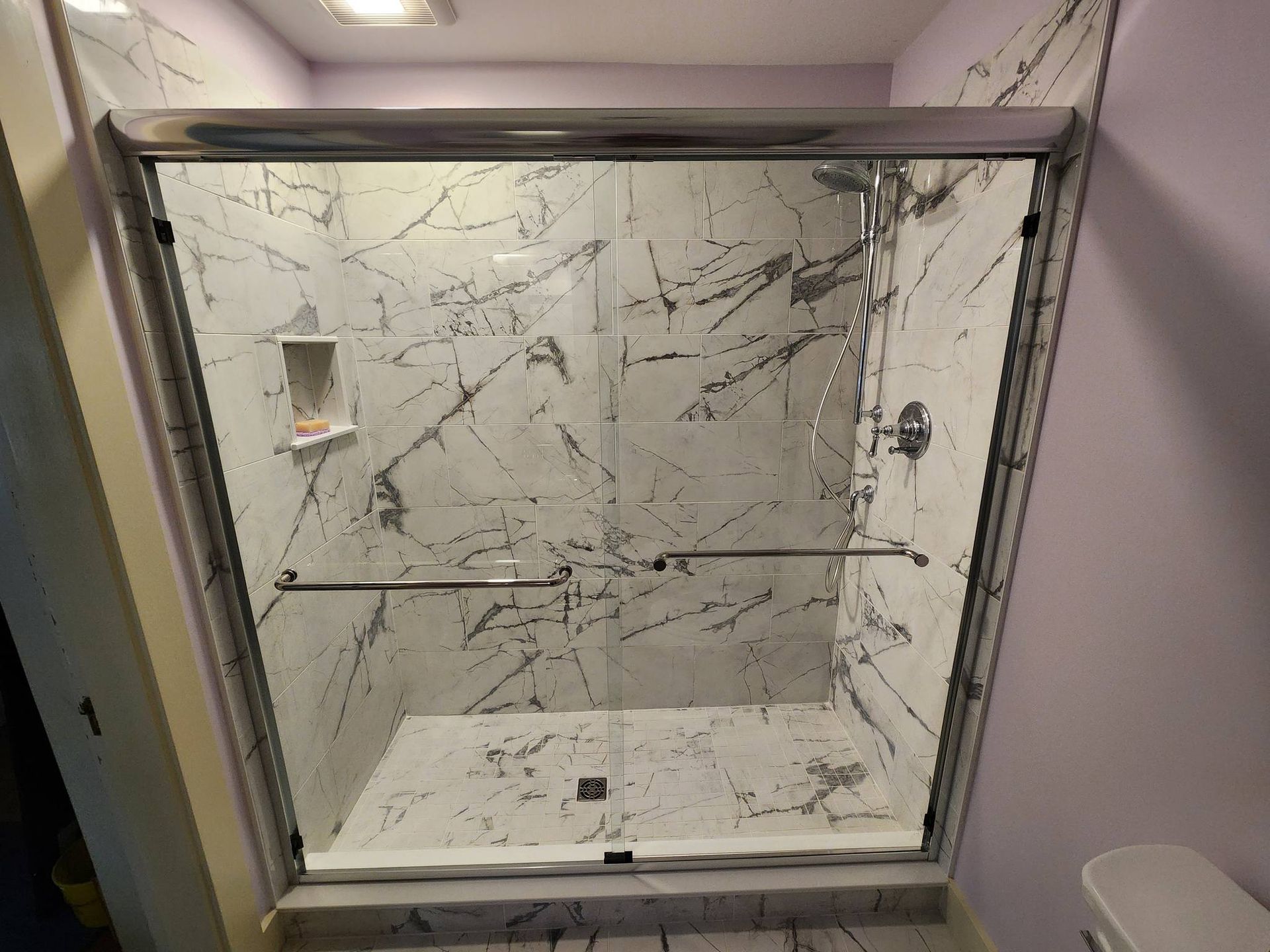 A bathroom with marble tiles and a sliding glass shower door.