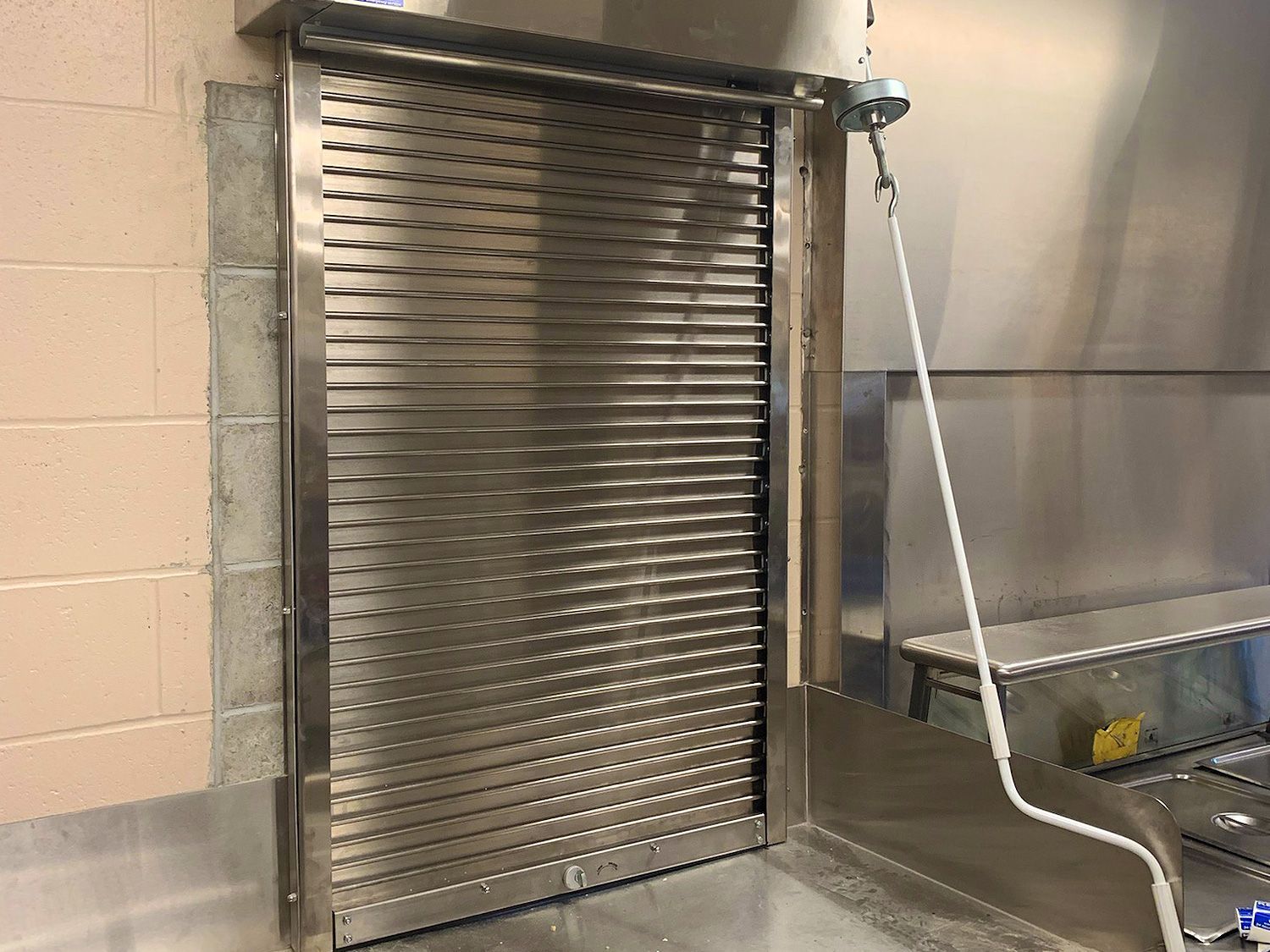 A stainless steel shutter is hanging on a wall next to a sink.