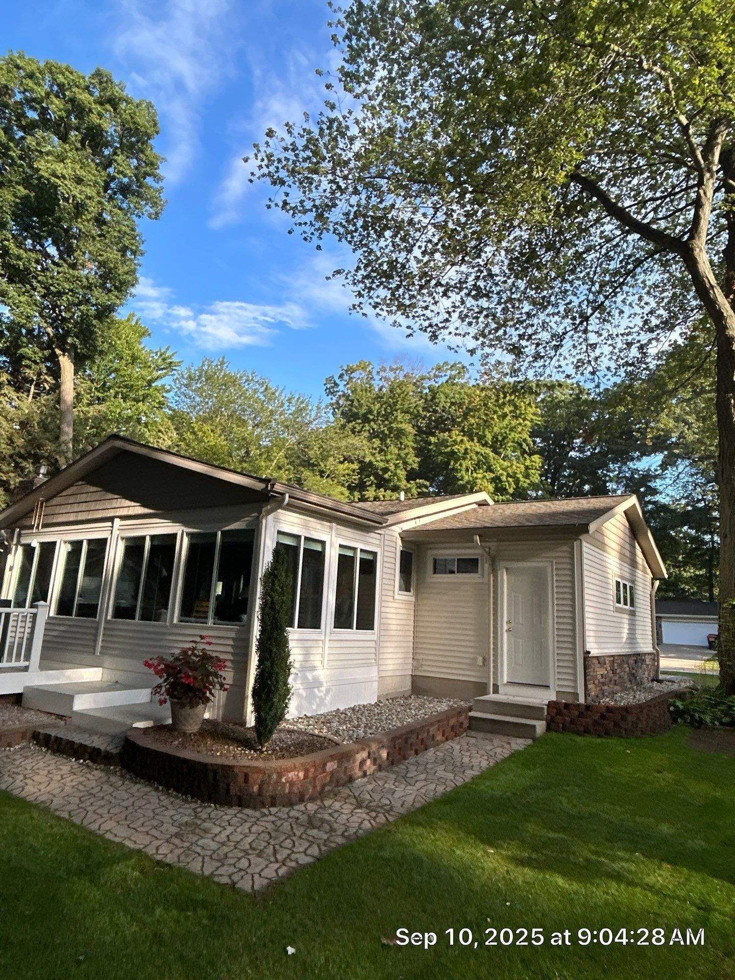 Cottage with a white exterior, surrounded by trees and lush green grass on a sunny day.