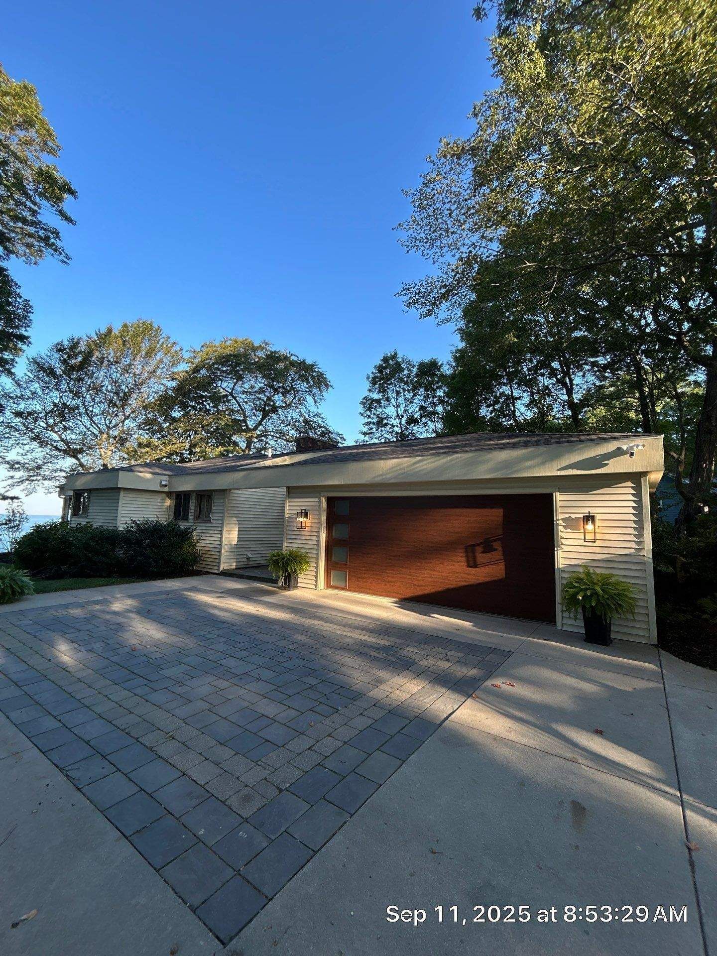 House with brown garage door, light siding, and brick driveway under blue sky.