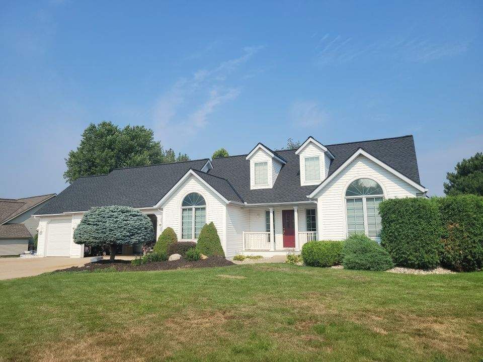 White house with black roof, red front door, and manicured landscaping under a blue sky.
