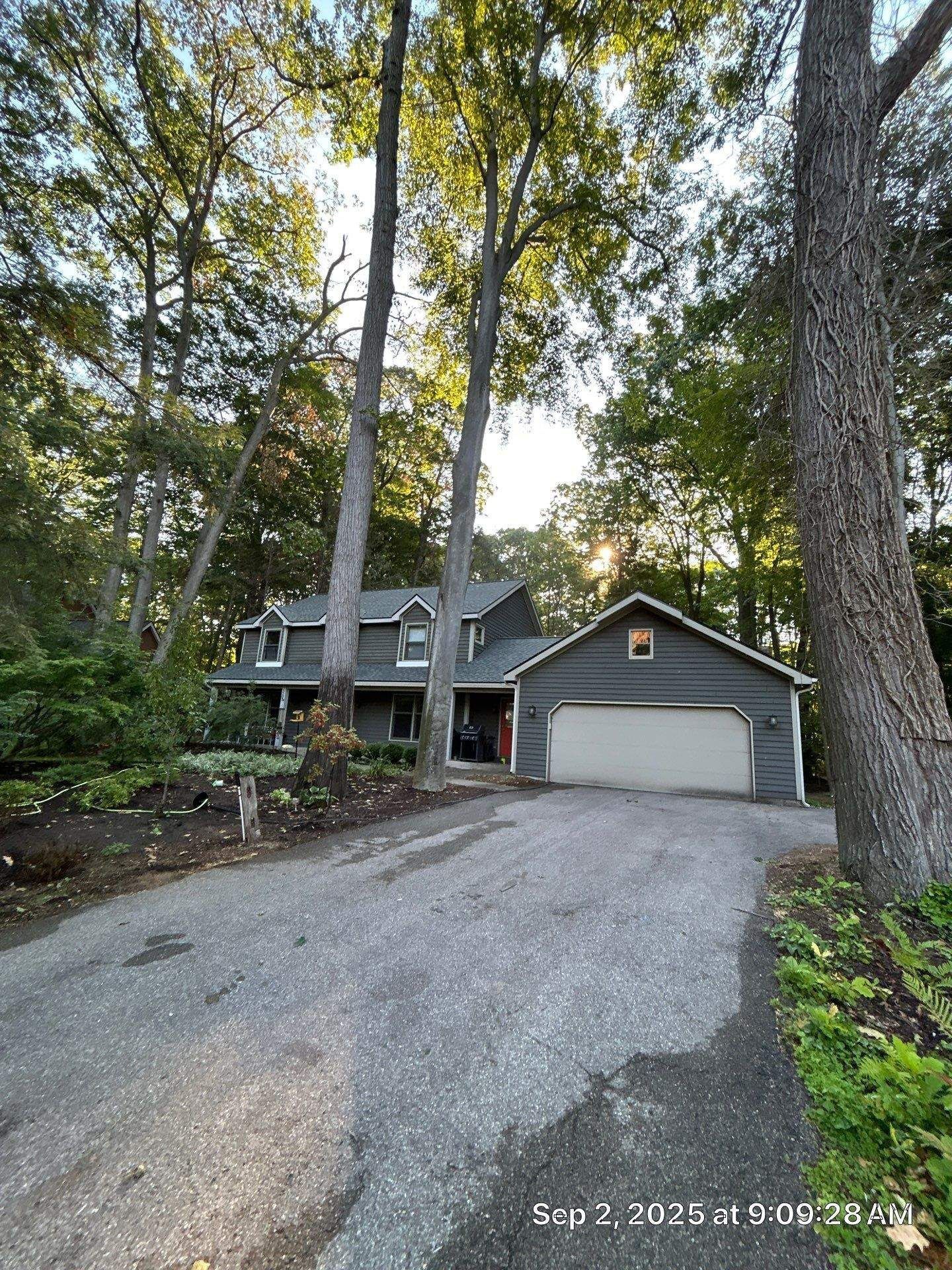 House with gray siding and white garage door, nestled amongst trees on a paved driveway.