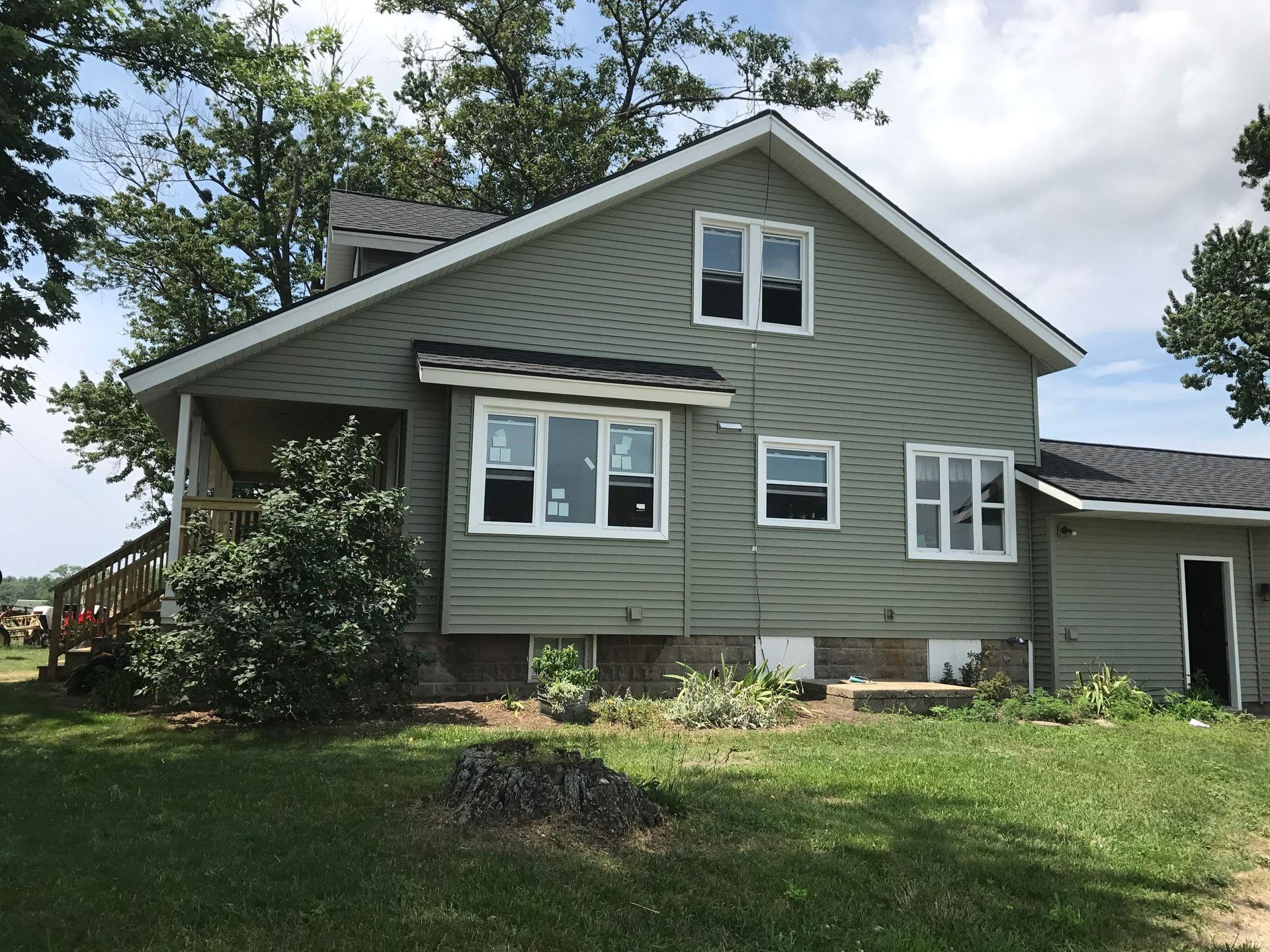 Green house with white trim, a porch, and a lawn under a blue sky.