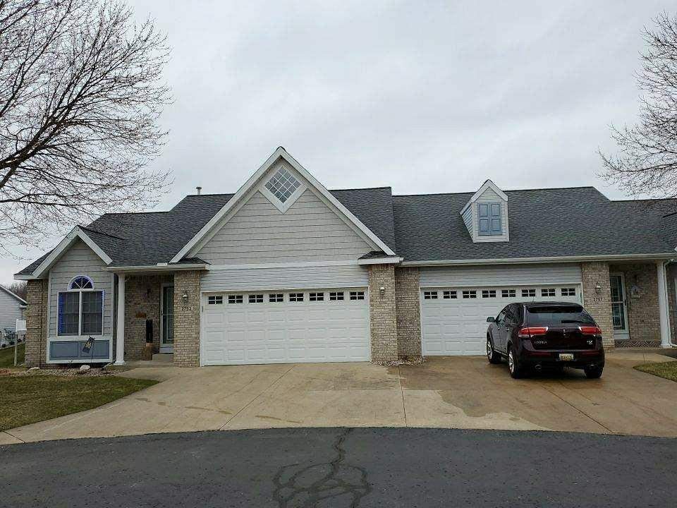 Townhouses with white garage doors and a car parked in the driveway on an overcast day.