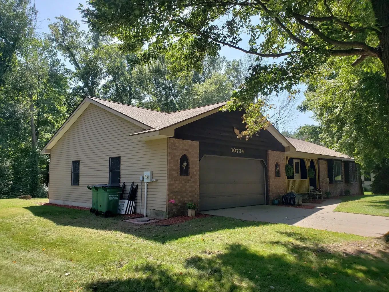 Tan ranch-style house with attached garage and green lawn, shaded by trees.
