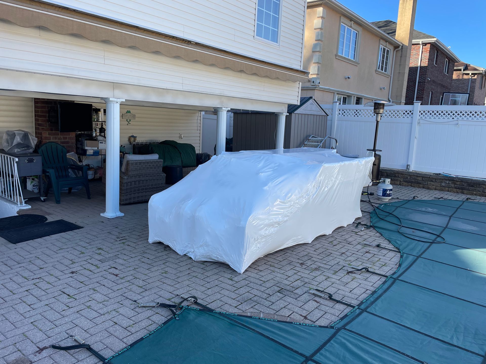 A couch is wrapped in plastic on a patio next to a pool