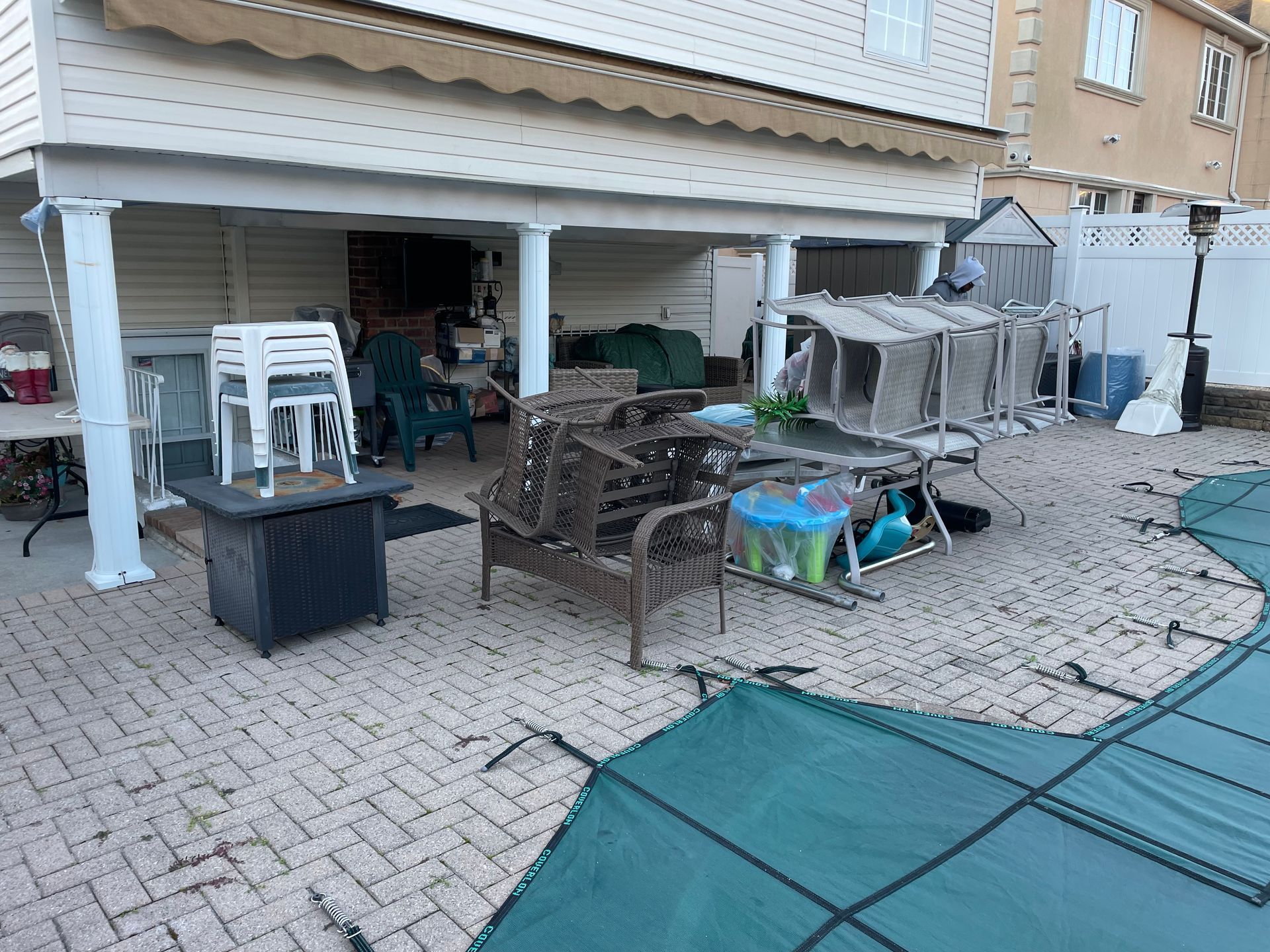 A patio with a fire pit, chairs, tables, and a pool cover