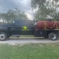 Black truck with large red tank in a grassy setting.