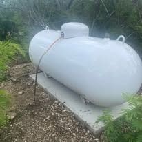 Large, white propane tank on a concrete base, outdoors near greenery.