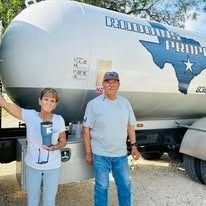 Woman and man with propane truck; woman holds a thermos, smiling.