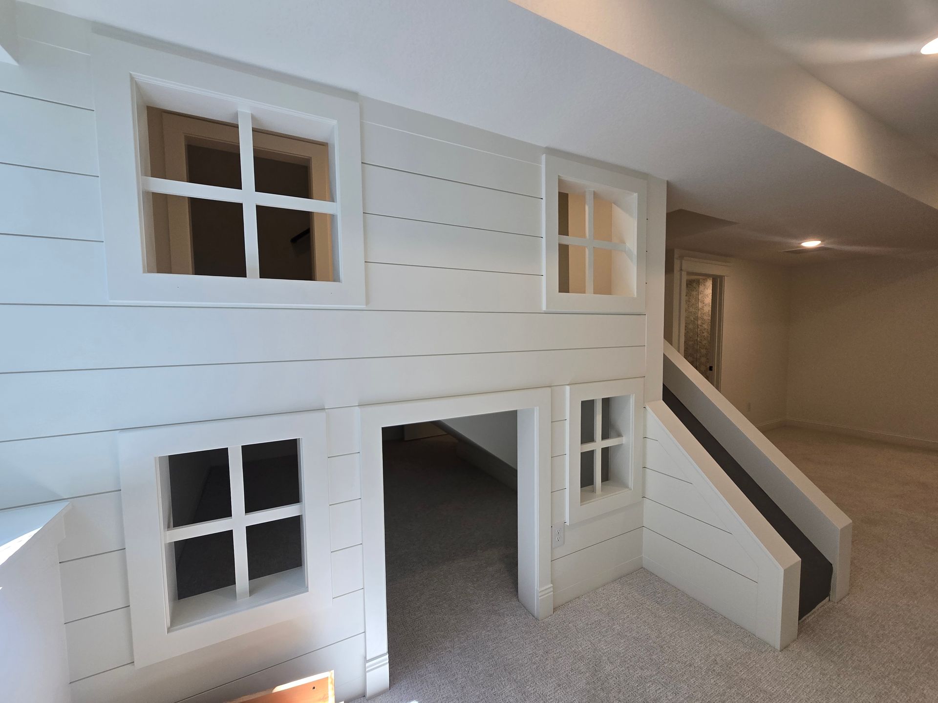 White playhouse structure with windows and a slide in a brightly lit room.