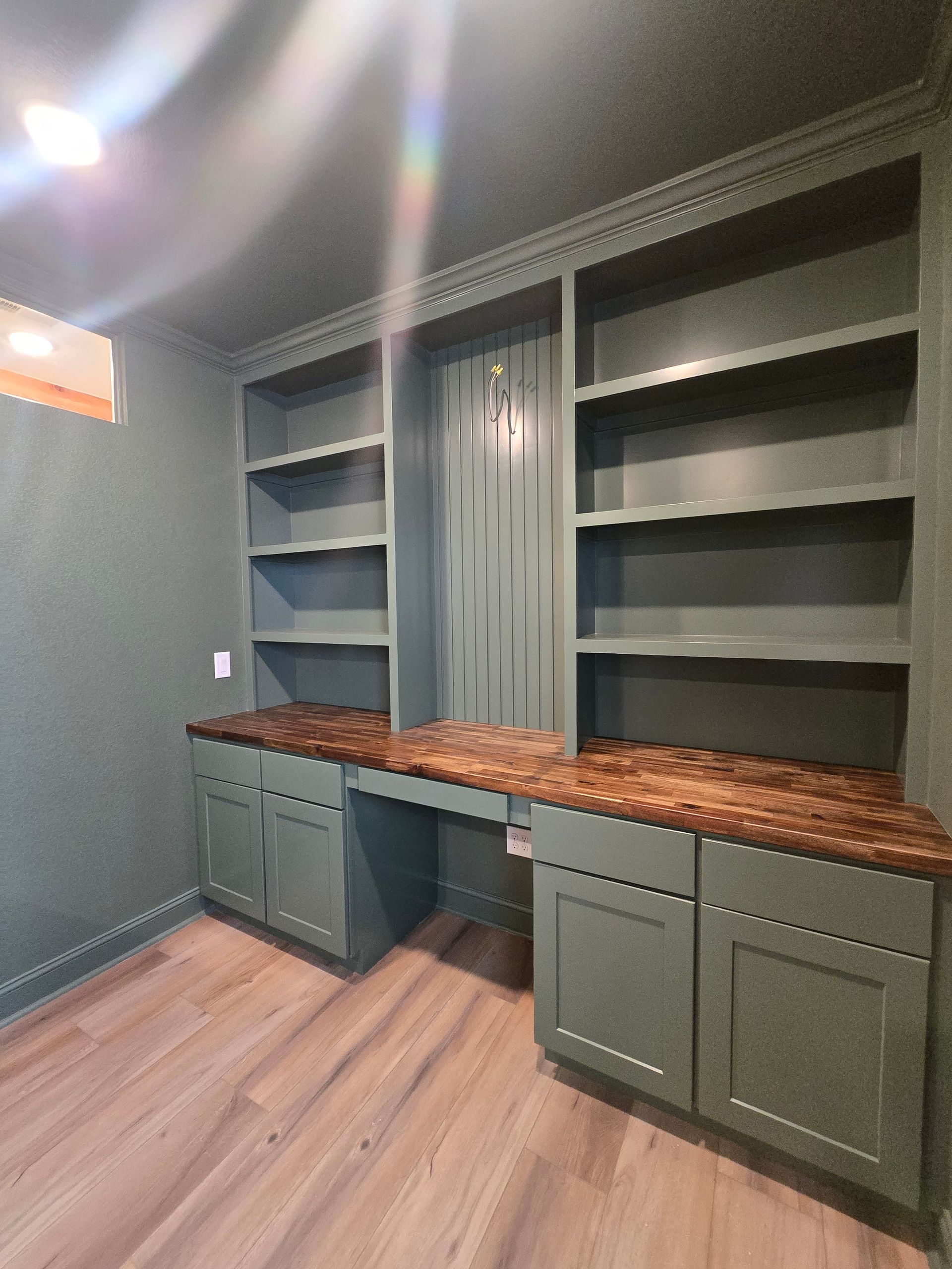 Built-in home office with green cabinets, dark wood desk, and matching bookshelves. The room has wood-look flooring.