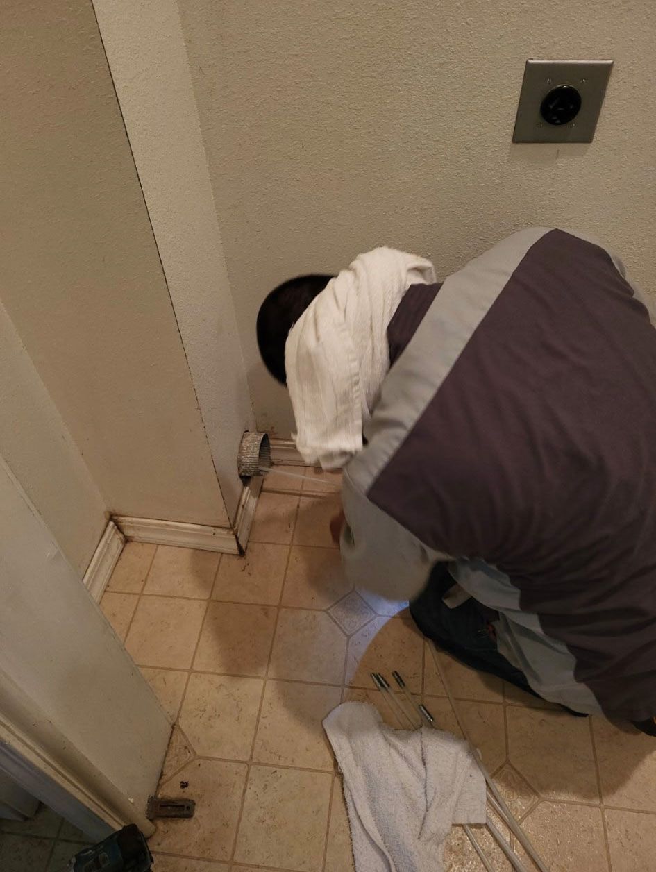 Person crouched on a tiled floor, working near a wall corner with a towel and cleaning supplies.