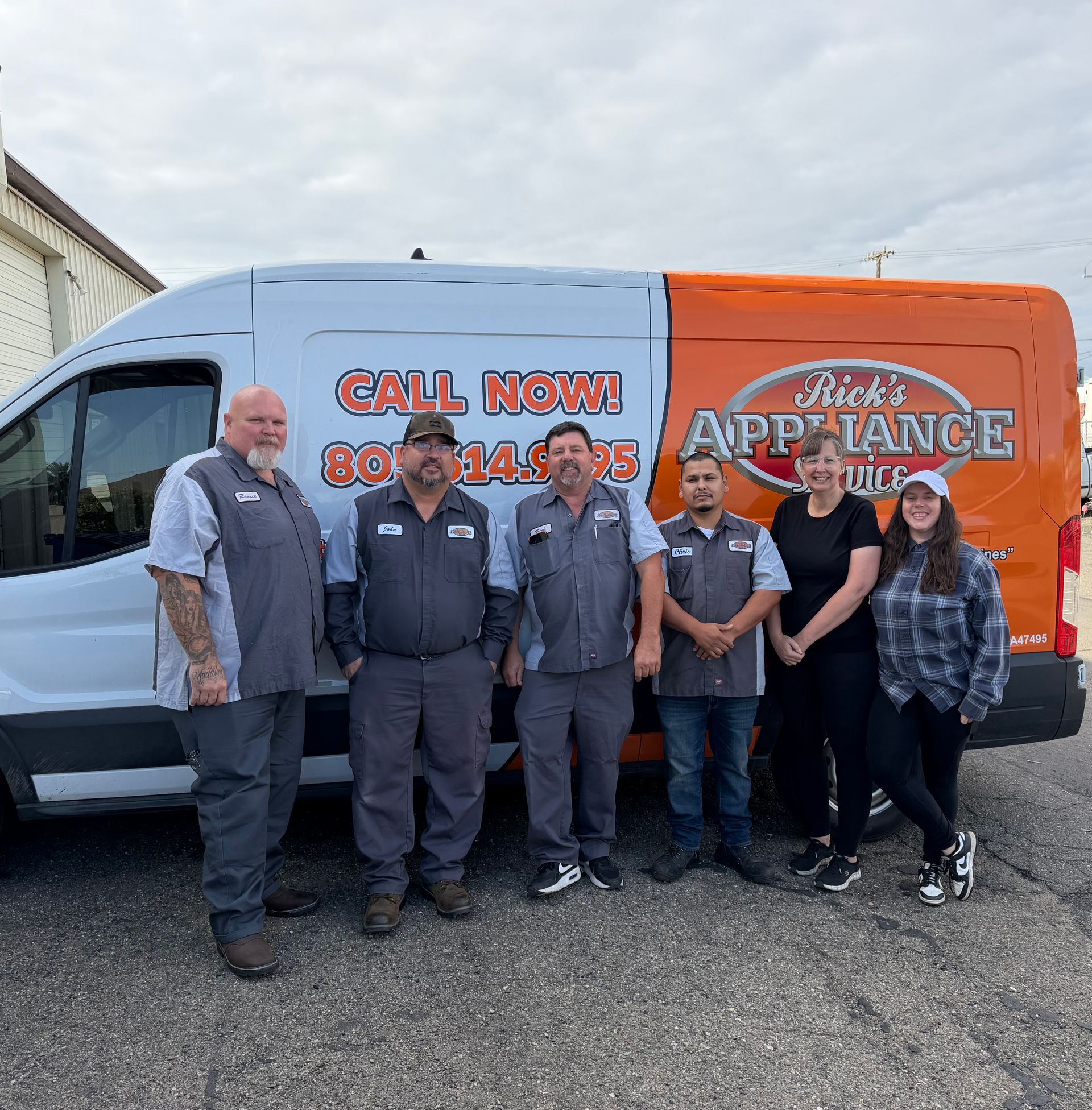 Six people posing in front of an orange and white moving truck with “Call Now!” signage.