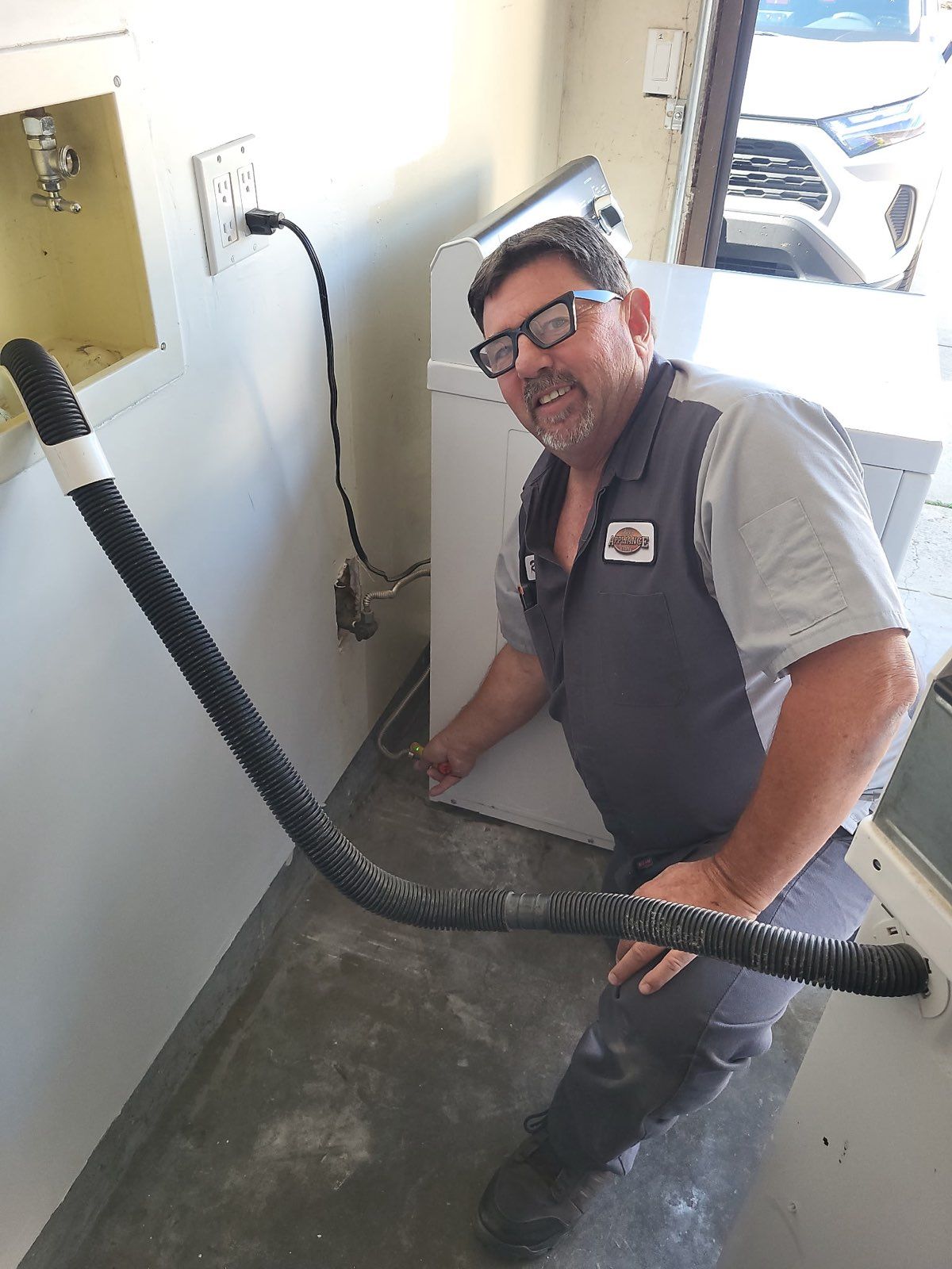 Worker cleaning a floor with a vacuum hose in a small utility room, smiling near an open doorway.