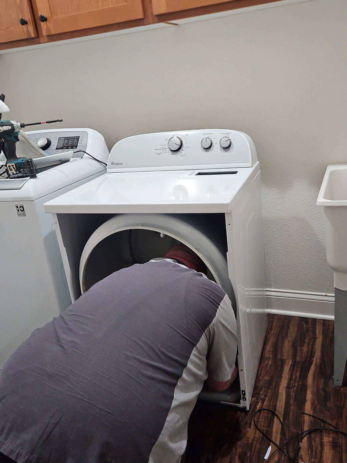 Person loading a white dryer in a laundry room with wood flooring.