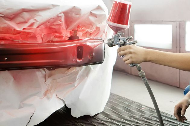Spray painting a red car bumper in a paint booth, with a hand holding a spray gun.