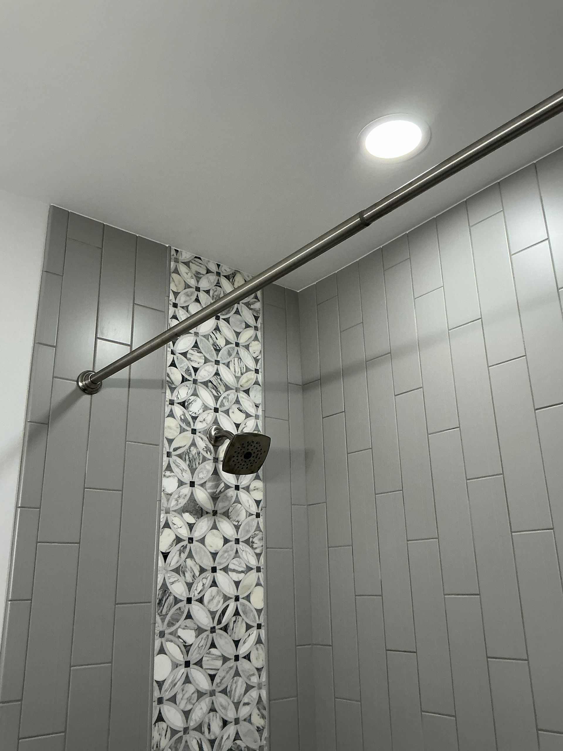 Modern shower with gray tile walls, decorative mosaic strip, and chrome shower rod.