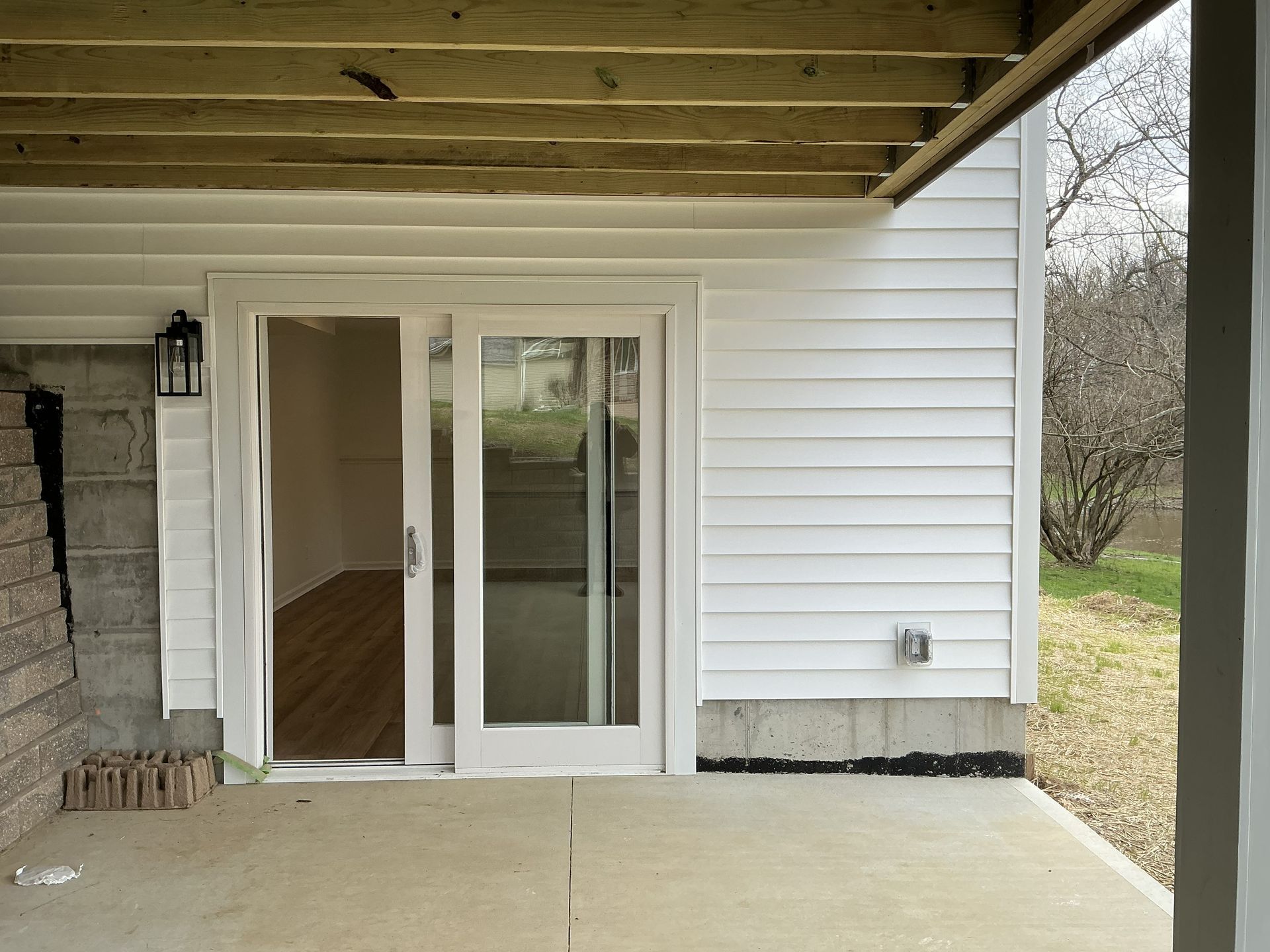 Covered patio with white sliding glass doors and adjacent siding leading to a grassy yard