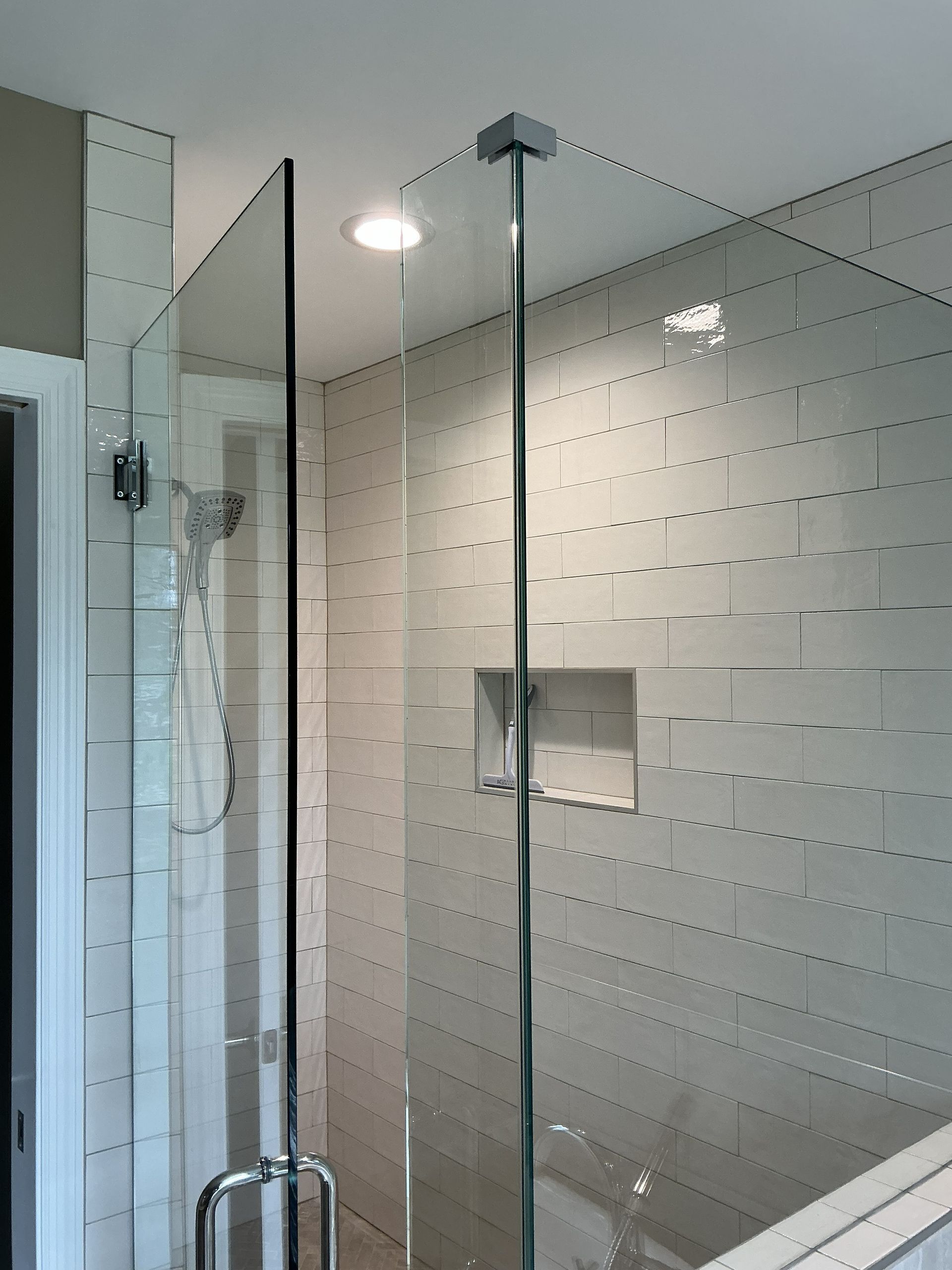 Modern bathroom shower with glass enclosure, white tiled walls, and chrome fixtures.