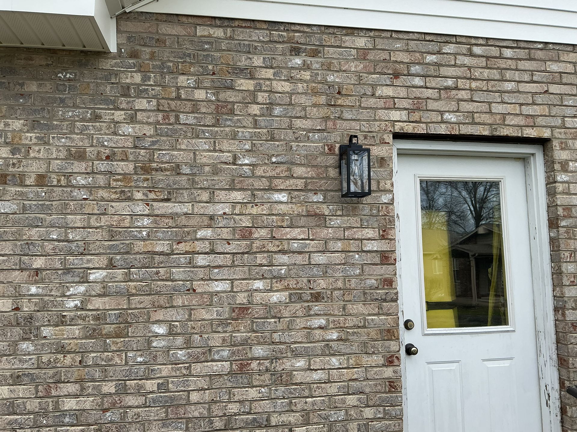 Brick house exterior with a white front door and wall-mounted lantern.