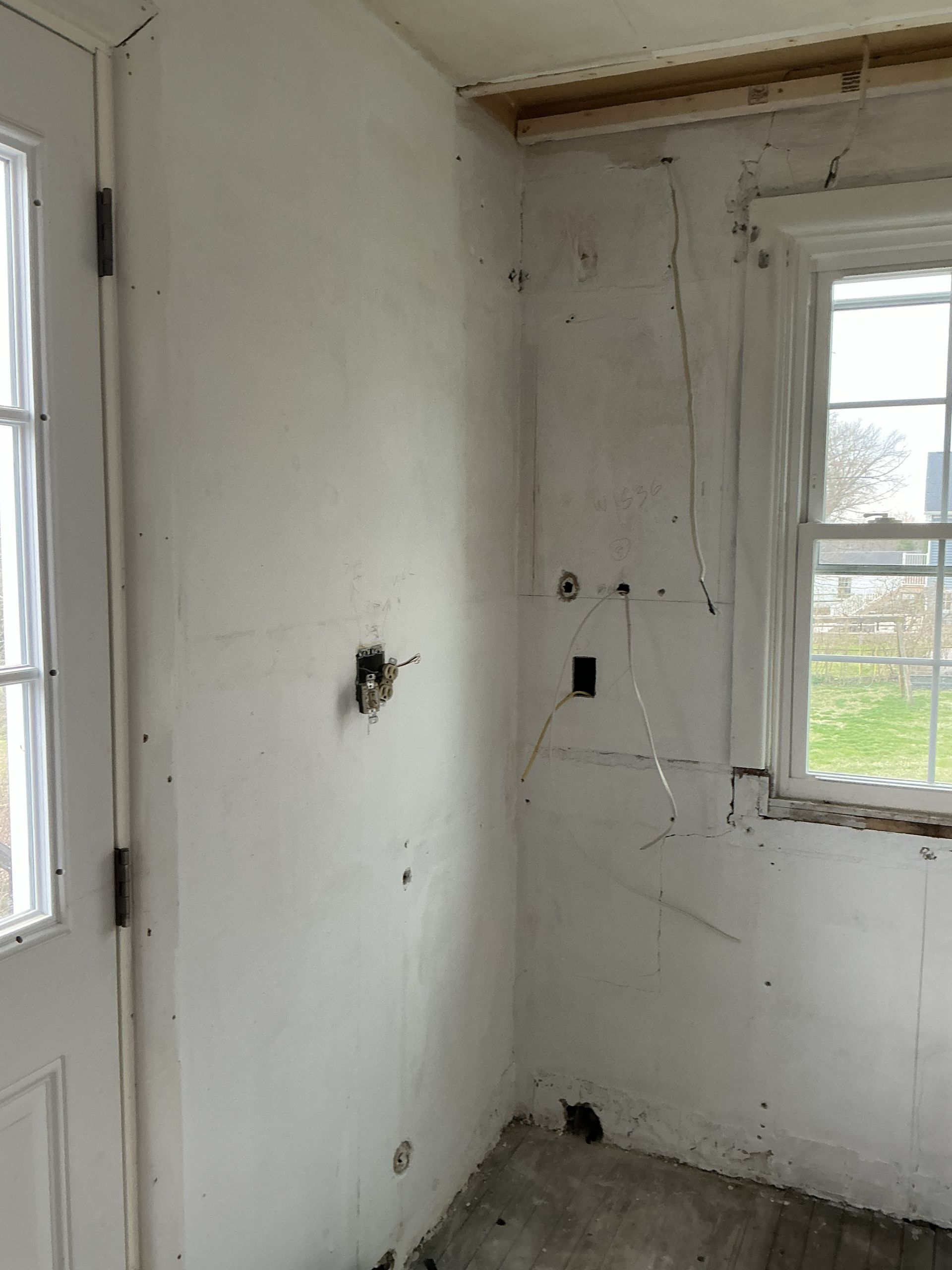 Small empty white room with a window and exposed electrical outlets.
