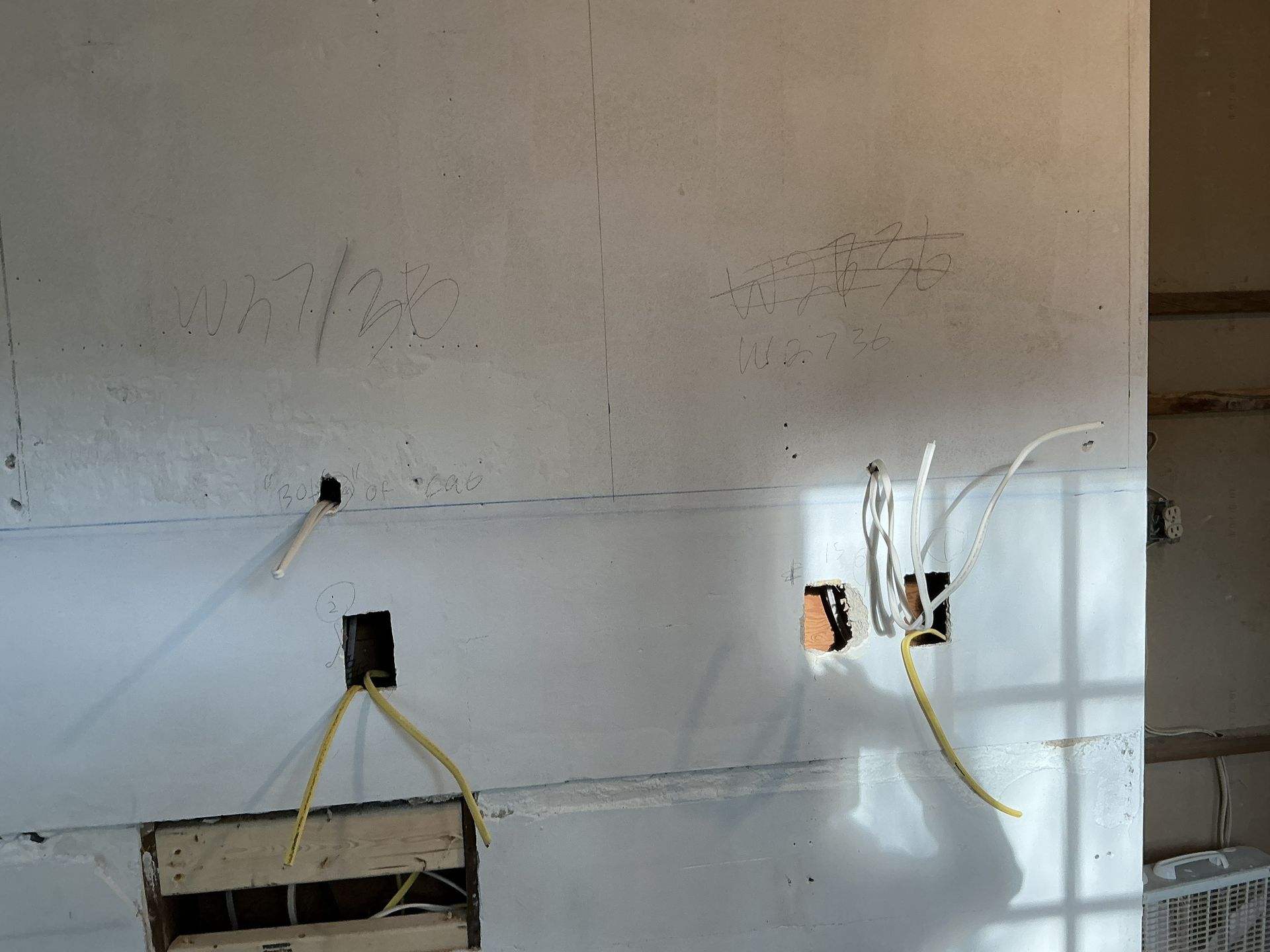 Unfinished drywall with exposed electrical boxes and yellow wiring in a wall cavity