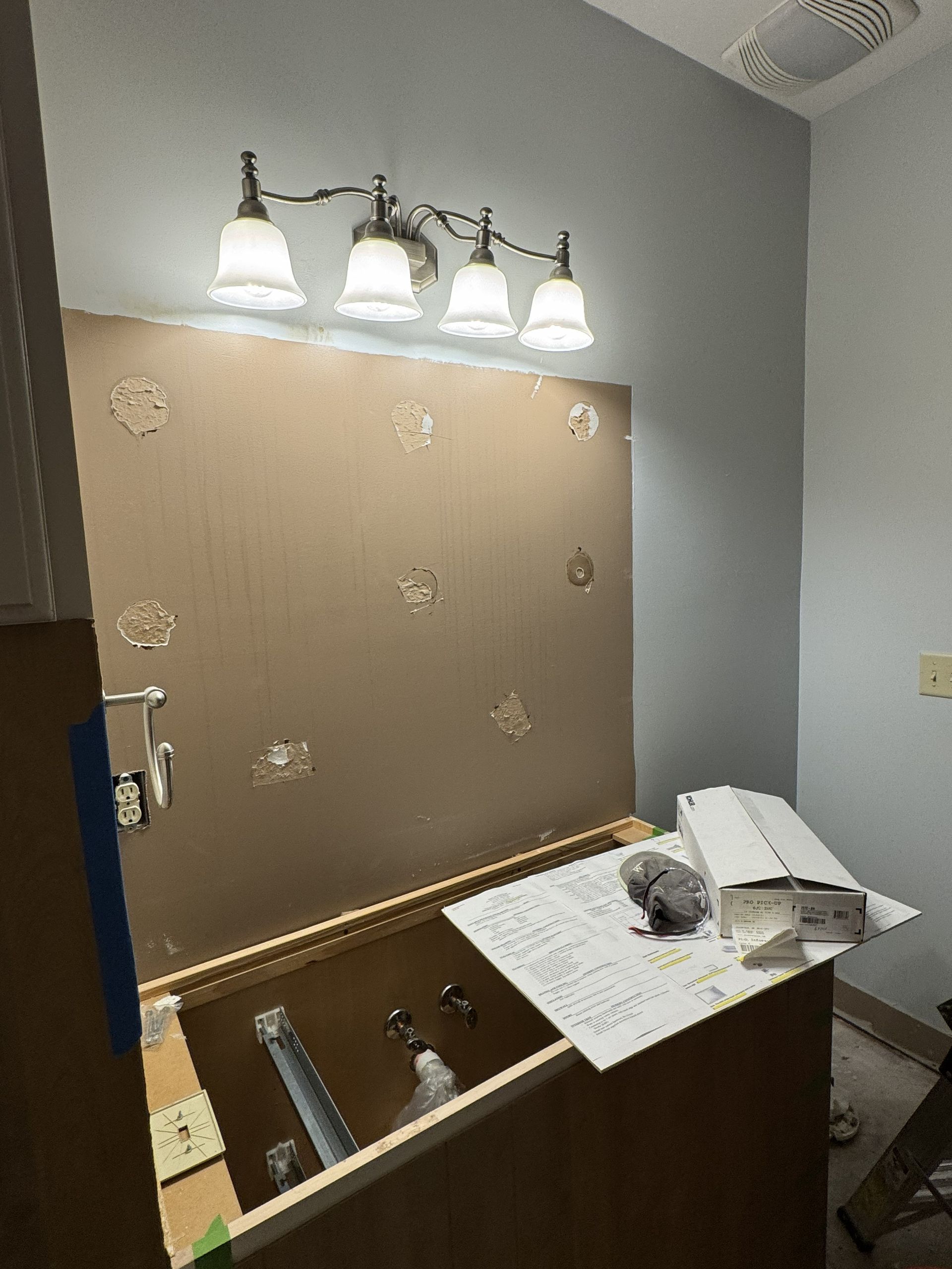 Bathroom vanity with lit three-light mirror, beige wallpaper, and sink area under renovation