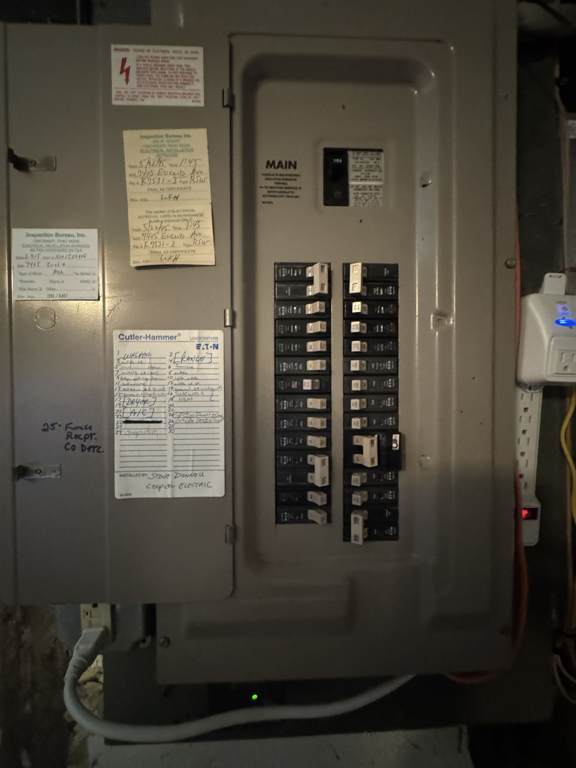 Electrical breaker panel with labeled circuits and notices on a gray wall.