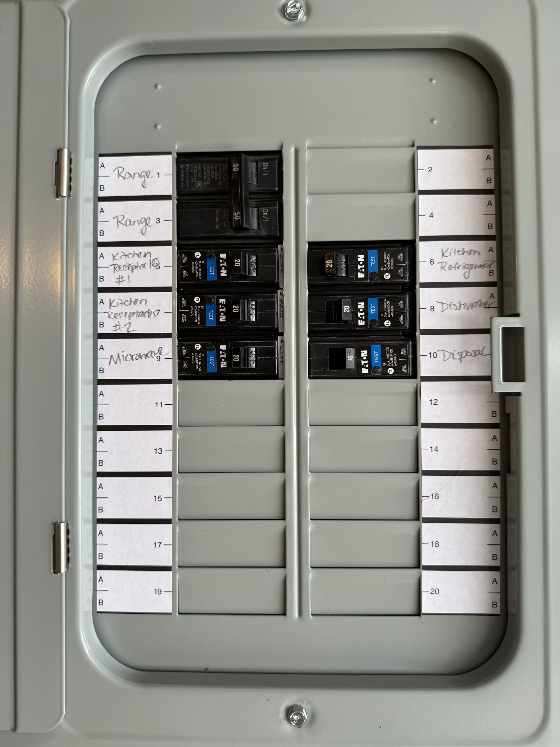 Electrical breaker panel with labeled switches and open cover in a gray metal cabinet