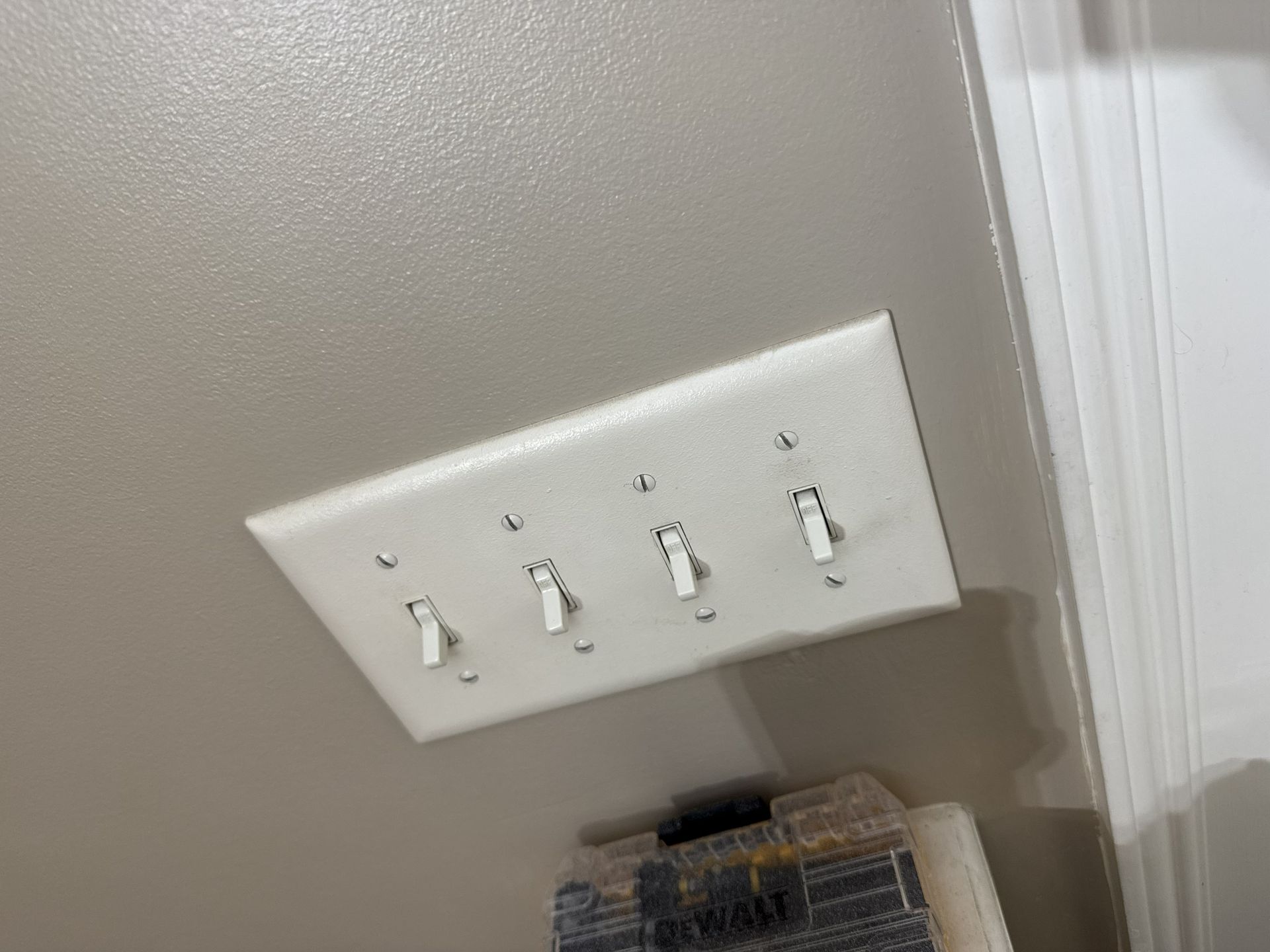 Tilted white 4-switch wall plate on beige wall above a basket or shelf.