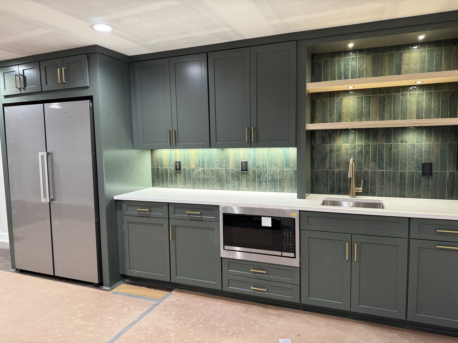 Modern kitchen with dark gray cabinets, stainless refrigerator, under-cabinet lighting, and glass display shelves