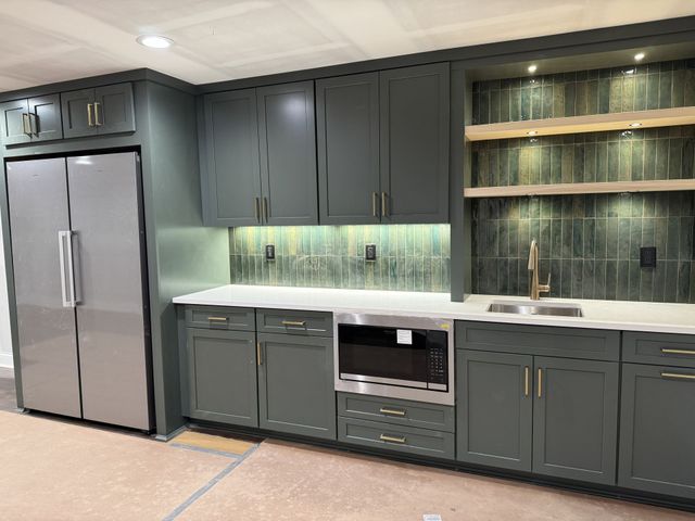 Modern kitchen with dark cabinets, stainless fridge, white countertop, and glass display shelves.