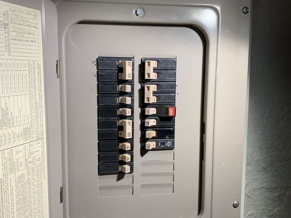 Electrical breaker panel with rows of switches inside a gray metal cabinet.