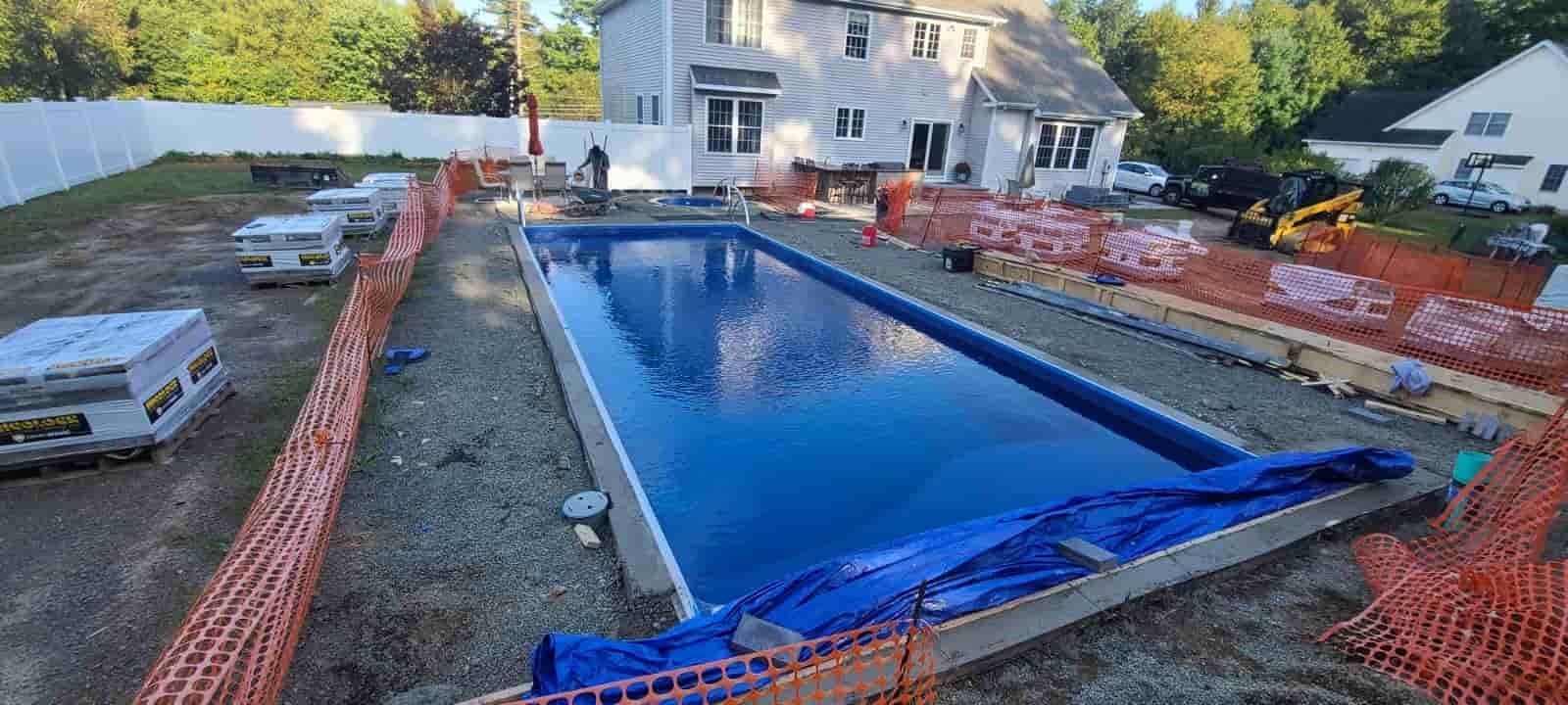 Backyard pool under construction with blue liner, orange safety fencing, and a house in the background