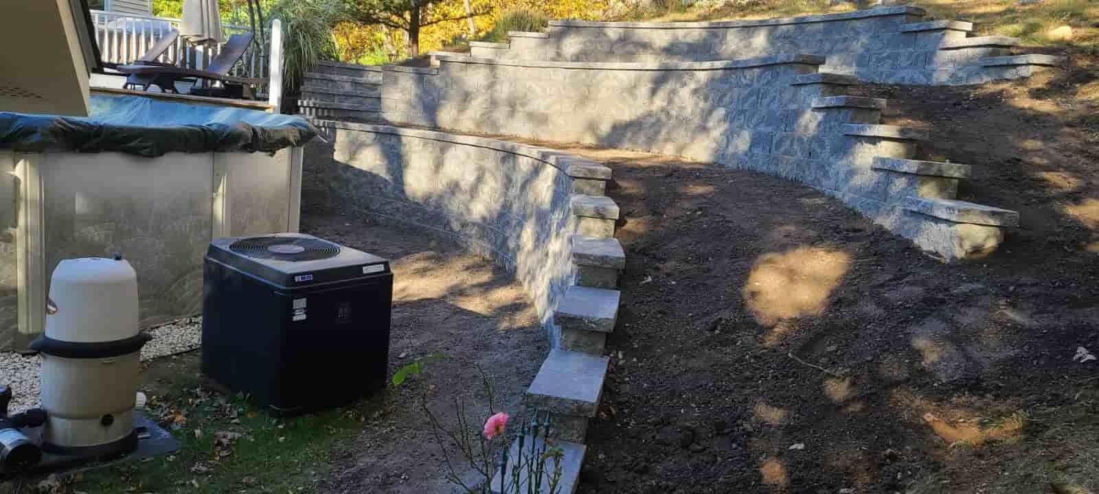 Backyard with stone steps, small retaining wall, and outdoor equipment beside a concrete patio